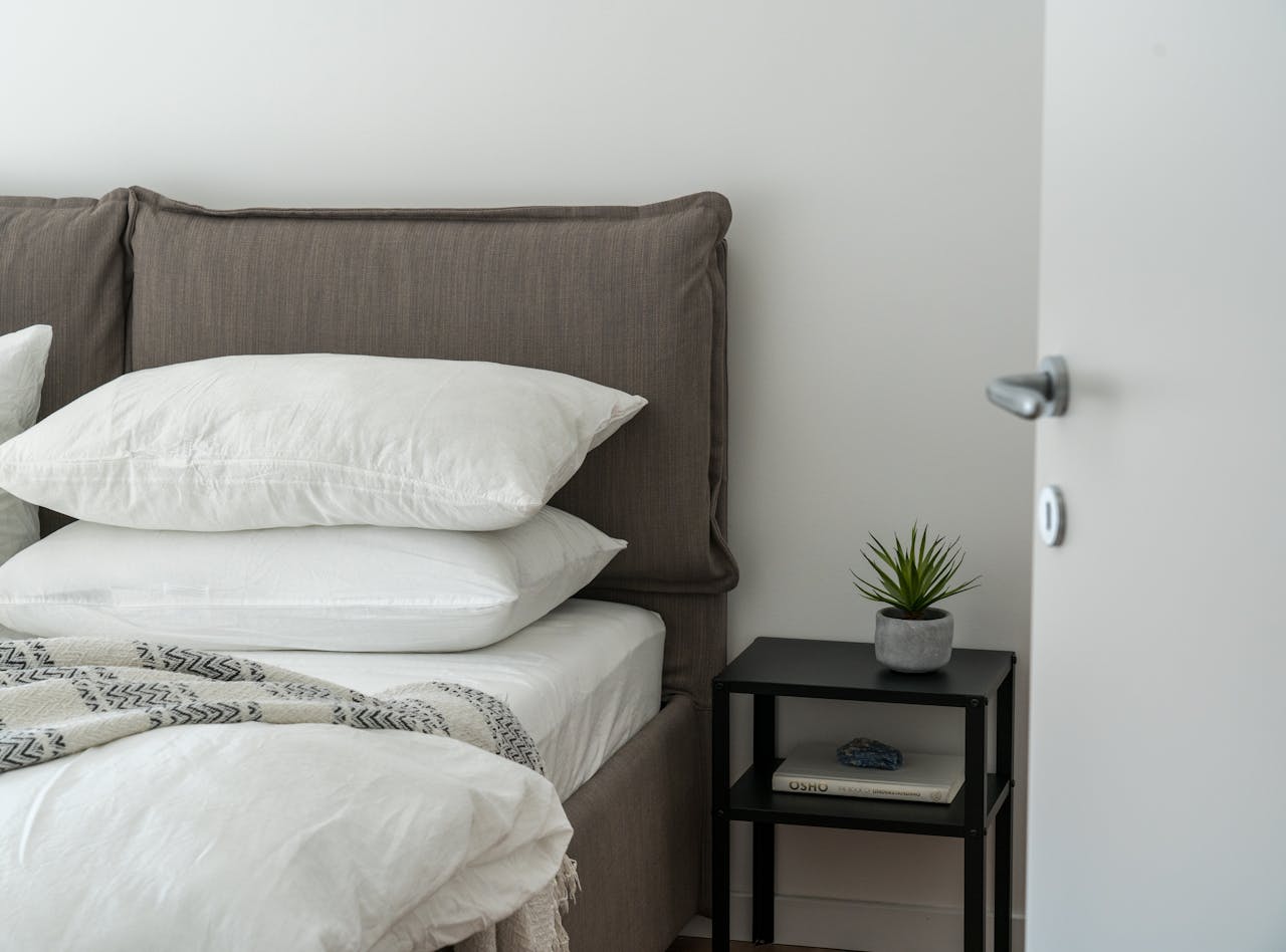 about-us A serene and stylish bedroom featuring a comfortable bed with clean white bedding and a side table with decor.